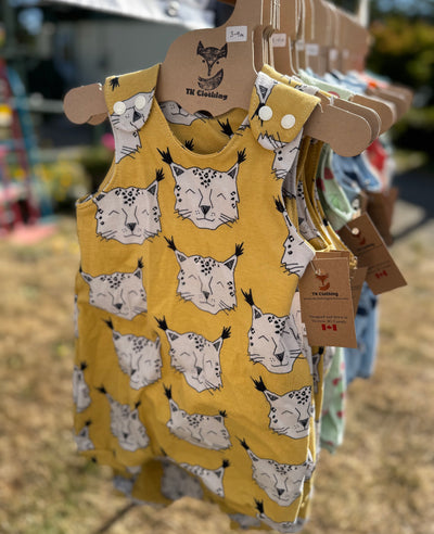 Yellow romper with a cute cartoon bobcat pattern on a hanger at an outdoor market.