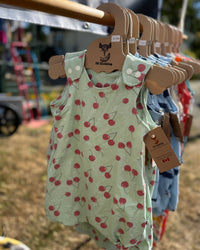 Children's romper with cherry pattern on a hanger at an outdoor market.