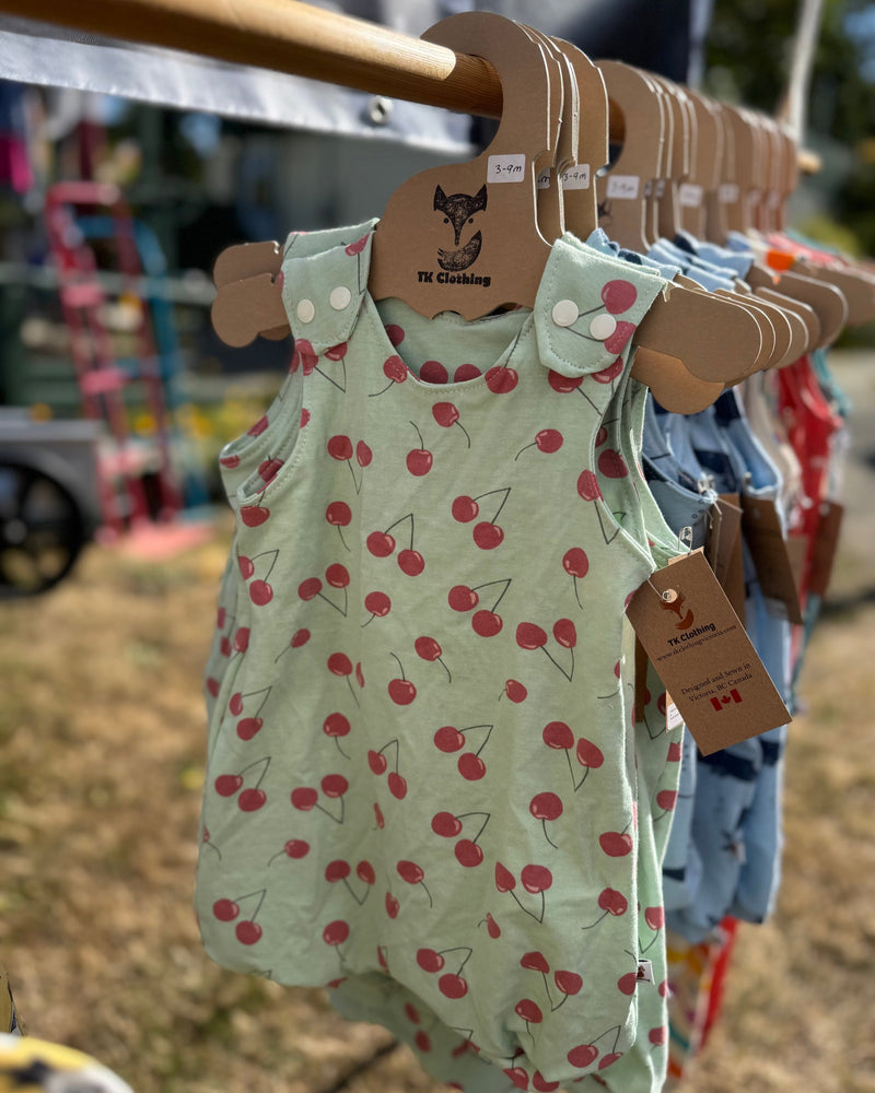 Children's romper with cherry pattern on a hanger at an outdoor market.