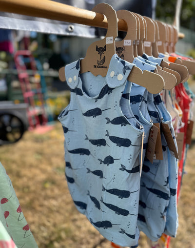 Children's rompers with whale pattern on hangers against a blurred outdoor background