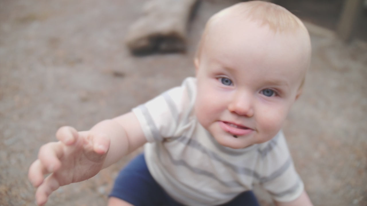 Close-up of a happy baby wearing a striped short-sleeve Merino wool top and navy merino shorts, crawling and playing in a park to demonstrate freedom of movement. Clothes made by TK Clothing